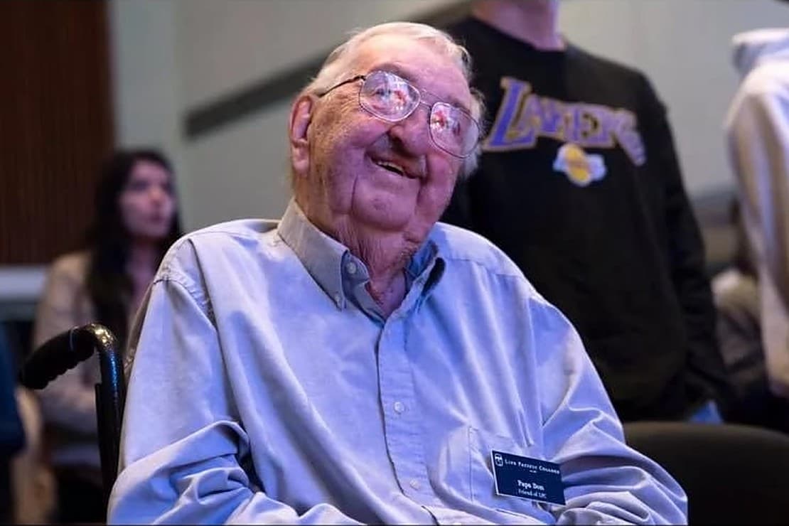 Papa Don, an older man in a wheelchair wearing a name tag, smiling up at a gathering of college students